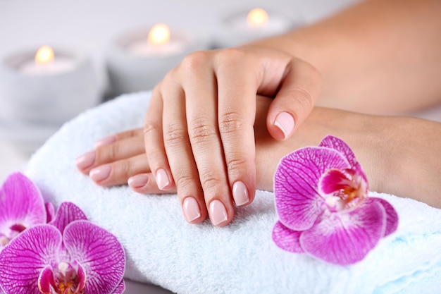 Woman hands with french manicure and orchid flowers on wooden table closeup