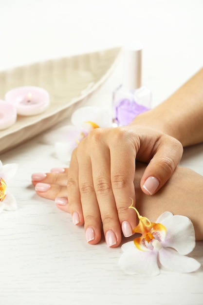 Photo woman hands with french manicure and orchid flowers on wooden table closeup