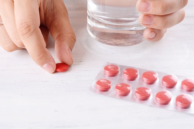 Woman hands with glass of water and pills.