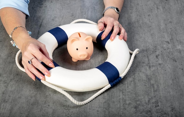 Woman hands with little piggy bank inside of lifebuoy safe\
money blue and white life buoy on wooden desk table background\
assets wealth money saving and security by insurance concept copy\
space
