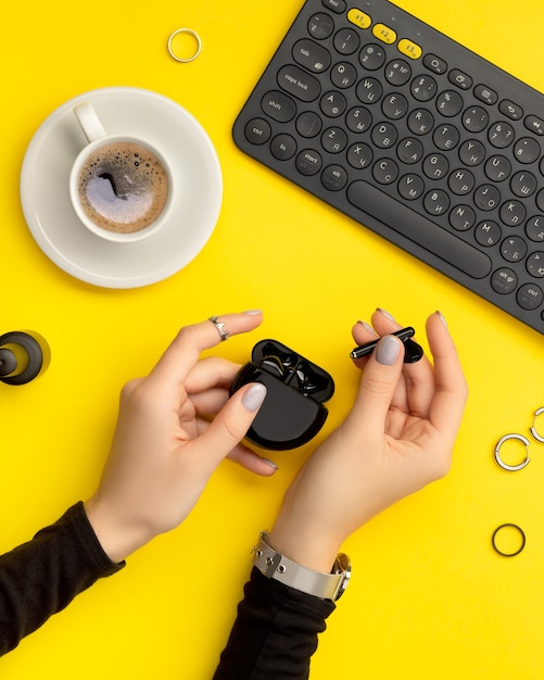 Woman hands with minimal manicure holding wireless headphones on yellow