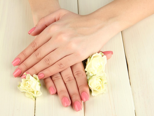 Woman hands with pink manicure and flowers on wooden background