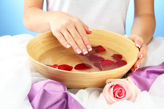 Woman hands with wooden bowl of water with petals on blue background