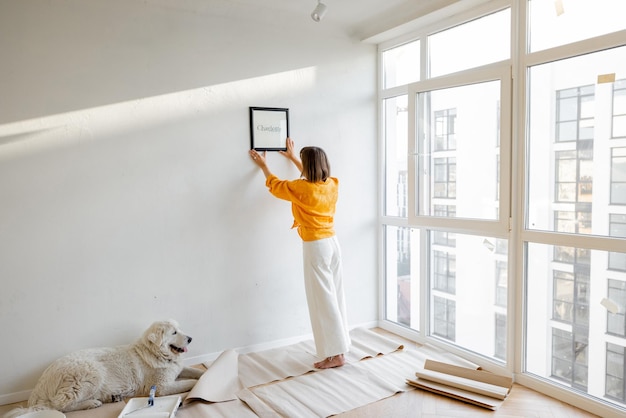 Woman hanging picture frame in newly renovated apartment