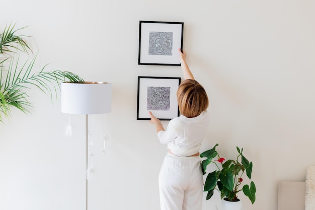 Woman hanging pictures on wall in room Interior design