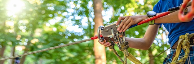 La donna appende un moschettone su una corda in un parco avventura forestale. utilizzo dell'attrezzatura da arrampicata: moschettone, cintura, corda. banner per pubblicità, design o intestazione del sito web