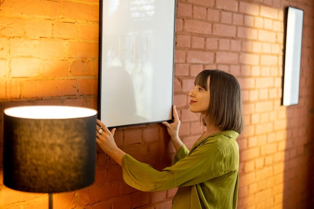 Woman hangs a photo frame on brick wall at home