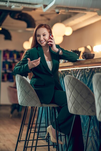Foto donna che parla felicemente sullo smartphone seduto nella caffetteria