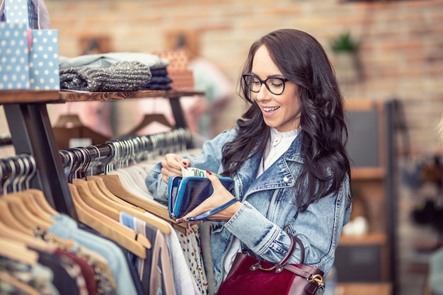 財布の中身に満足している女性は、衣料品店で購入する洋服を選びます。