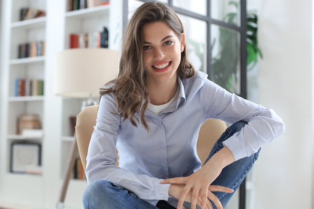 Woman happy on armchair smiling and stretching looking at camera.