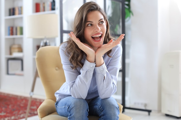 Woman happy on armchair smiling and stretching looking at camera.