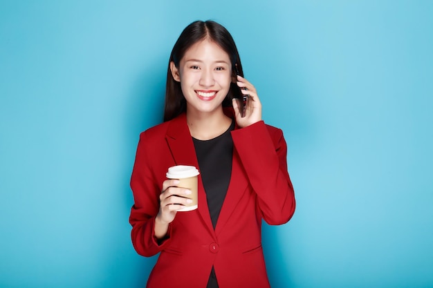 一人の肖像画の背景として青い背景を持つ女性が笑顔で携帯電話を手に持っています