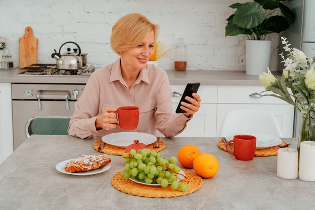 La donna fa colazione a casa con frutta, torta e caffè e legge le notizie dal suo smartphone