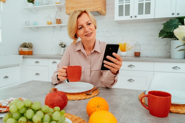 Woman has breakfast at home with fruitscake and coffee and reads news from smartphone