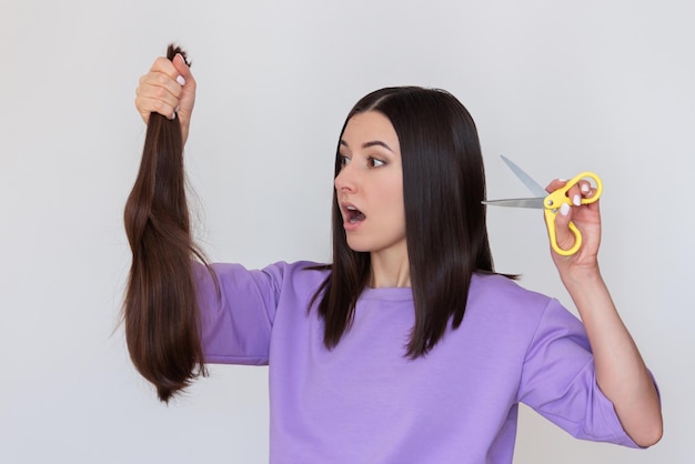 woman has cut off her long hair holds her cut hair in hand and looks at them with surprise