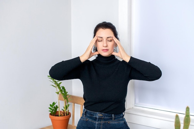 A woman has a headache sits on a chair and holds her head in her hands