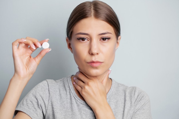 Woman has a sore throat and holds a pill for treatment