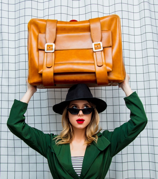 woman in hat and green cloak in 90s style with travel suitcase 