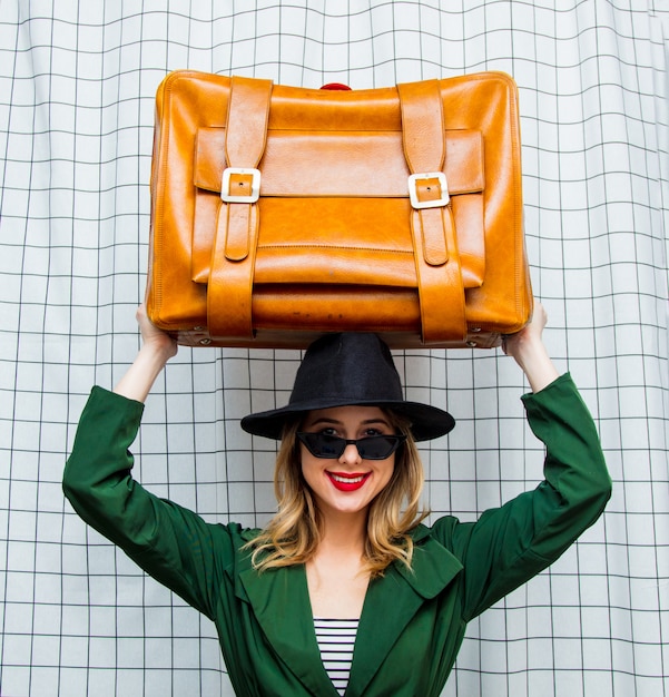 woman in hat and green cloak in 90s style with travel suitcase 