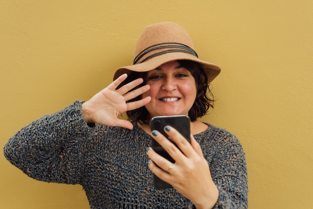 Woman in a hat greets on a video call, on a yellow background