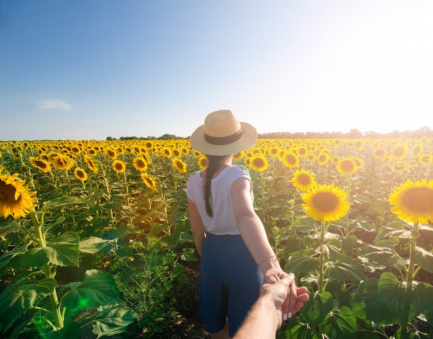 La donna in cappello sta tenendo a mano l'uomo che va al giacimento del girasole. viaggiando insieme. segui m