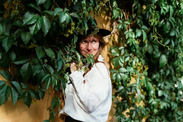 Woman in a hat near an old wall with hanging leaves