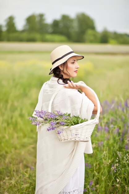 牧草地の枝編み細工品バスケットでライラックの花を摘む帽子の女。