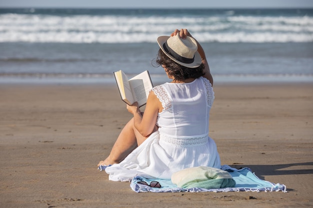 Woman in hat reading book on beach