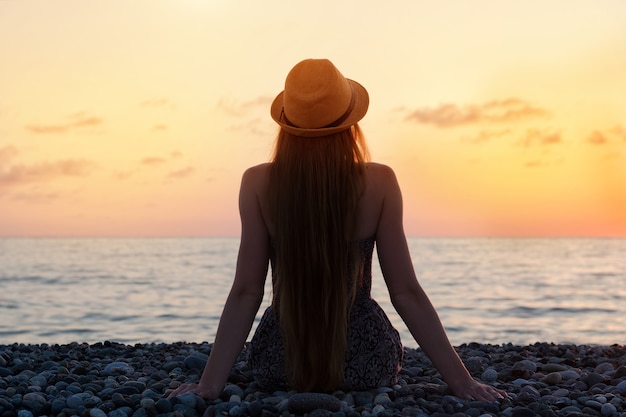 海岸に座っている帽子の女性。日没時間。シルエット。