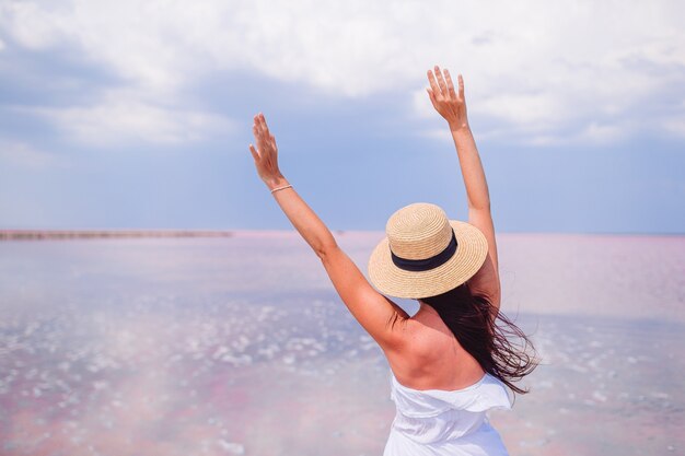 Woman in hat walk on a pink salt lake on a sunny summer day.