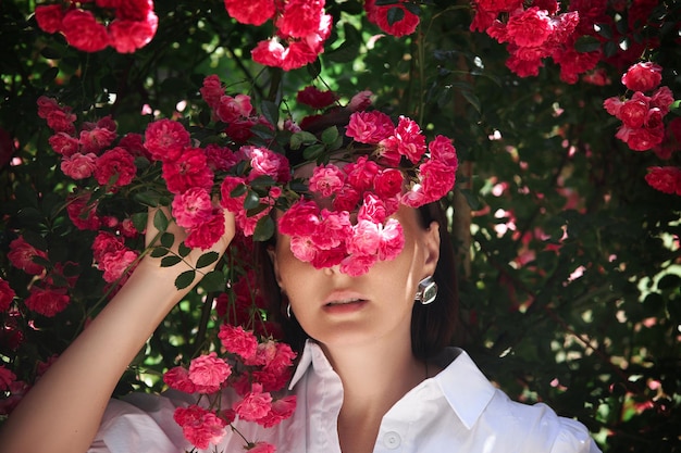 Foto donna in abito bianco e cappello passeggiate in giardino sullo sfondo di cespugli rosa bella ragazza romantica