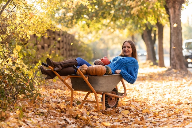 Woman have fun lying in the garden wheelbarrow with pumpkins