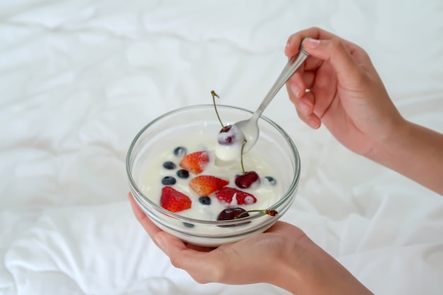 Donna che mangia una ciotola di yogurt con frutta fresca a letto.