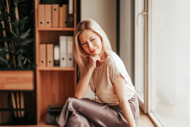 A woman having a break time relaxing at the office sitting at the windowsill