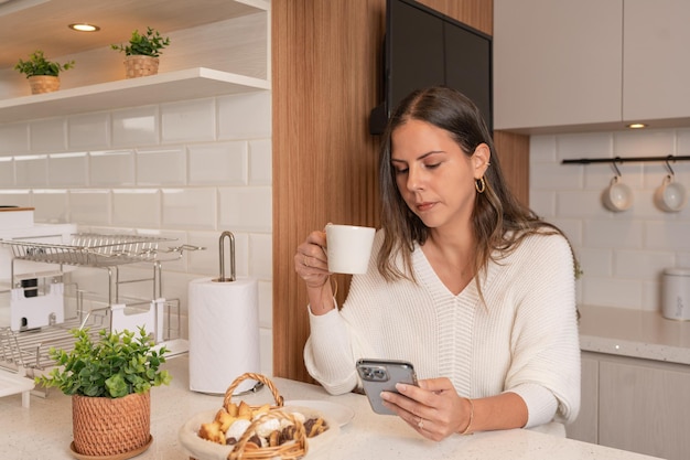 Женщина завтракает с помощью мобильного телефона на новой и современной кухне