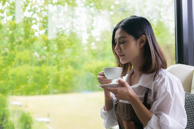 写真 カフェの窓のそばでコーヒーを飲んでいる女性