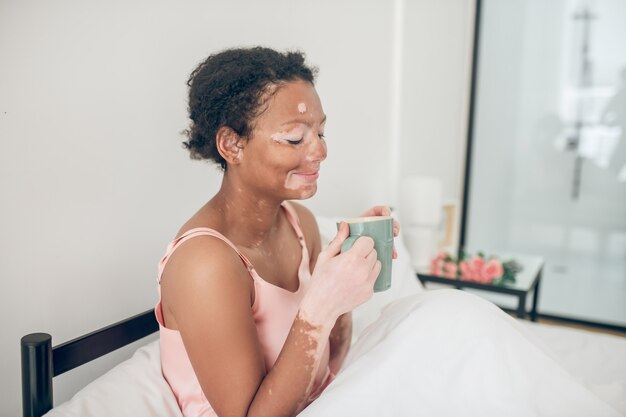 A woman having coffee in the morning while laying in bed