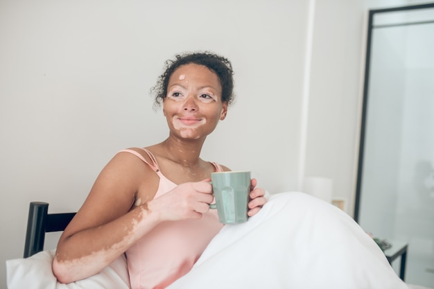 A woman having coffee in the morning while laying in bed