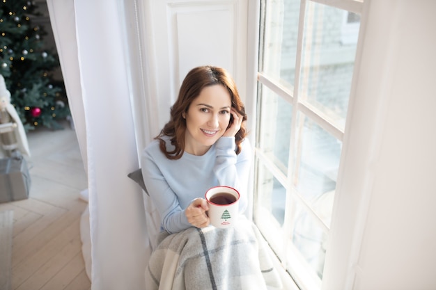 窓の近くでコーヒーを飲む女性