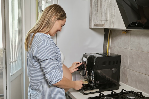 コーヒーマシンを使用して、キッチンでコーヒーを飲む女性