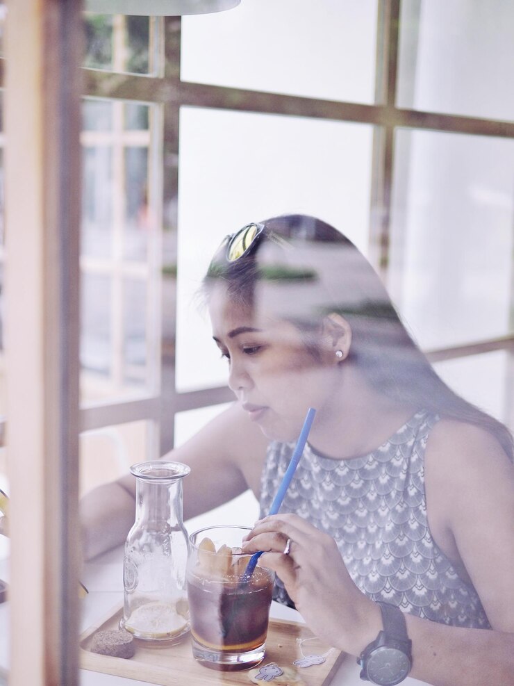 Photo ガラスの窓から見えるカフェで飲み物をしている女性