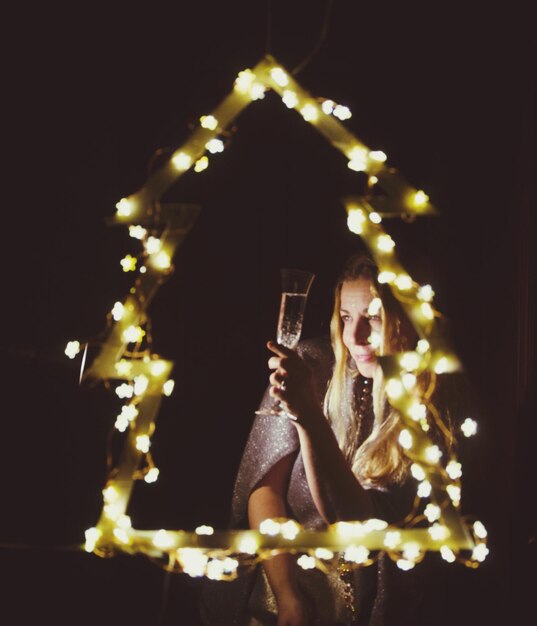 Woman having drink seen through christmas decoration against black background