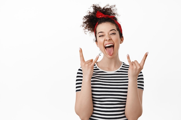 Photo woman having fun, show tongue and heavy metal horns gesture, feeling free and relaxed, standing over white