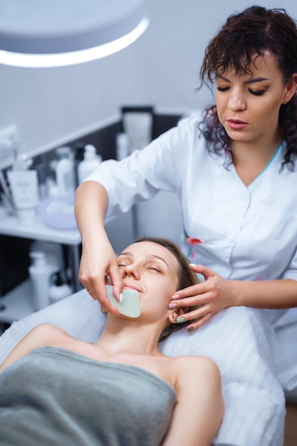 Woman having an gua sha facial massage with natural jade stone massager in the salon