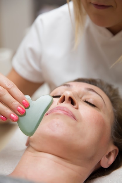 Woman having an gua sha facial massage with natural jade stone massager