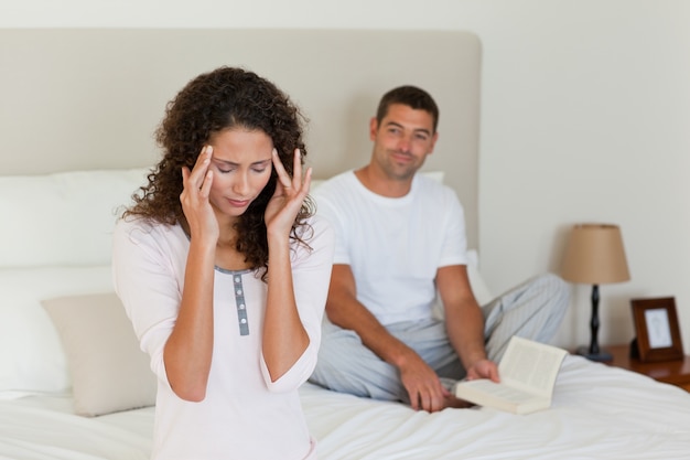 Woman having a headache while her husband is reading