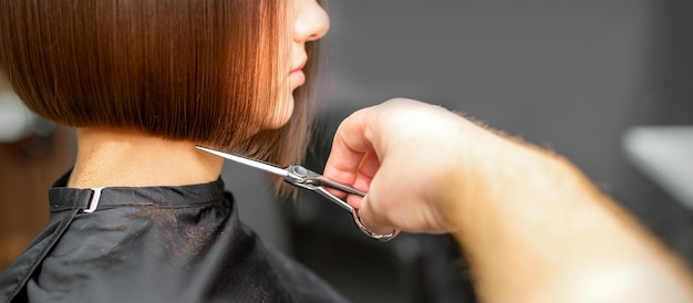 Donna che ha un nuovo taglio di capelli. parrucchiere maschio che taglia i capelli castani con le forbici in un parrucchiere.