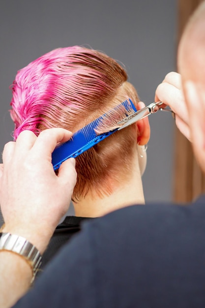 新しい散髪をしている女性。ヘアサロンでハサミでピンクのショートヘアをカットする男性のヘアスタイリスト。