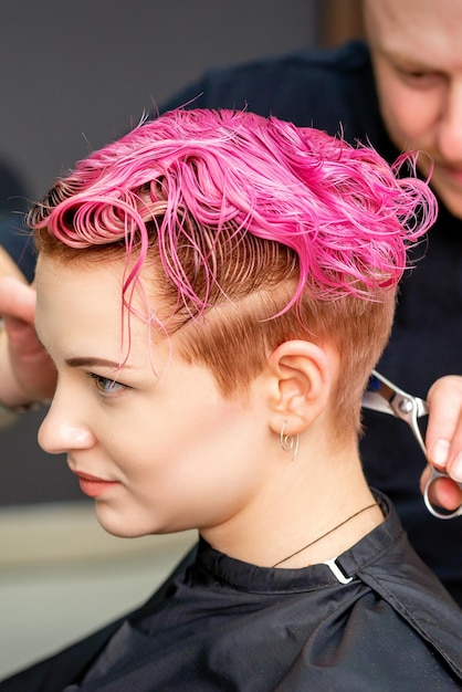 Foto donna che ha un nuovo taglio di capelli. un parrucchiere maschio sta tagliando i capelli corti rosa tinti con le forbici in un parrucchiere.