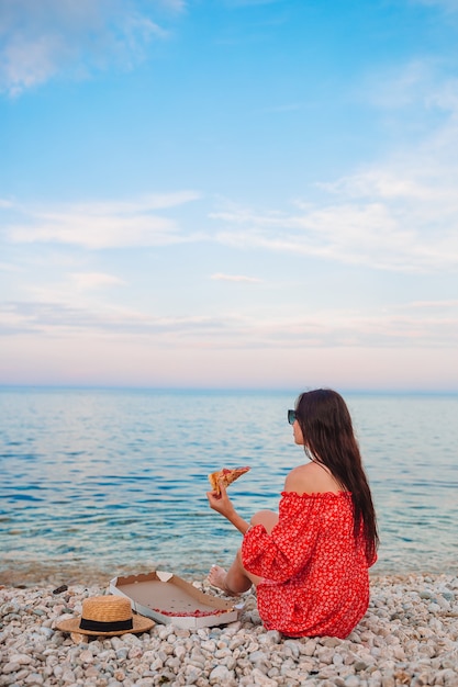 ビーチでピザとピクニックをしている女性